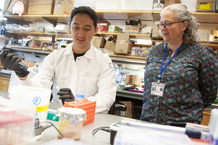 a man uses a pipet in a research lab while conversing with a woman scientist